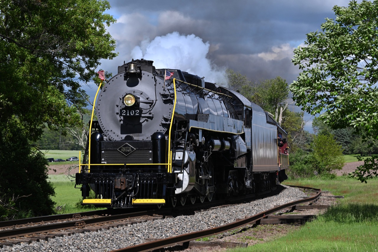 Reading and Northern steam locomotive 2102 rounding a curve between green trees.